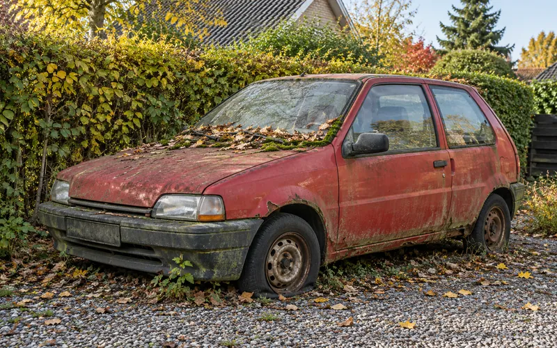 En gammel rød bil med rust og et fladt dæk, der har holdt stille længe