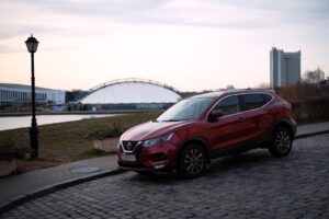 Rød Nissan Qashqai parkeret langs en brostensbelagt vej