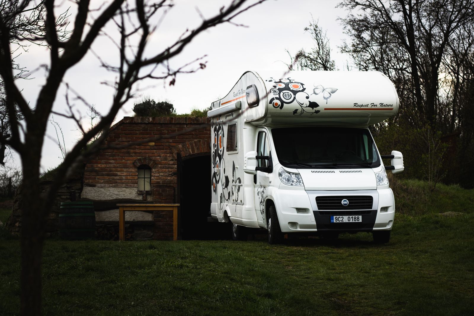 Hvid autocamper på Fiat-base parkeret ved en gammel murstensbygning